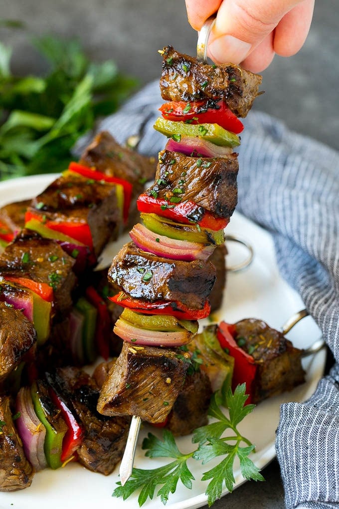 A hand holding a beef shish kabob with peppers and onions.