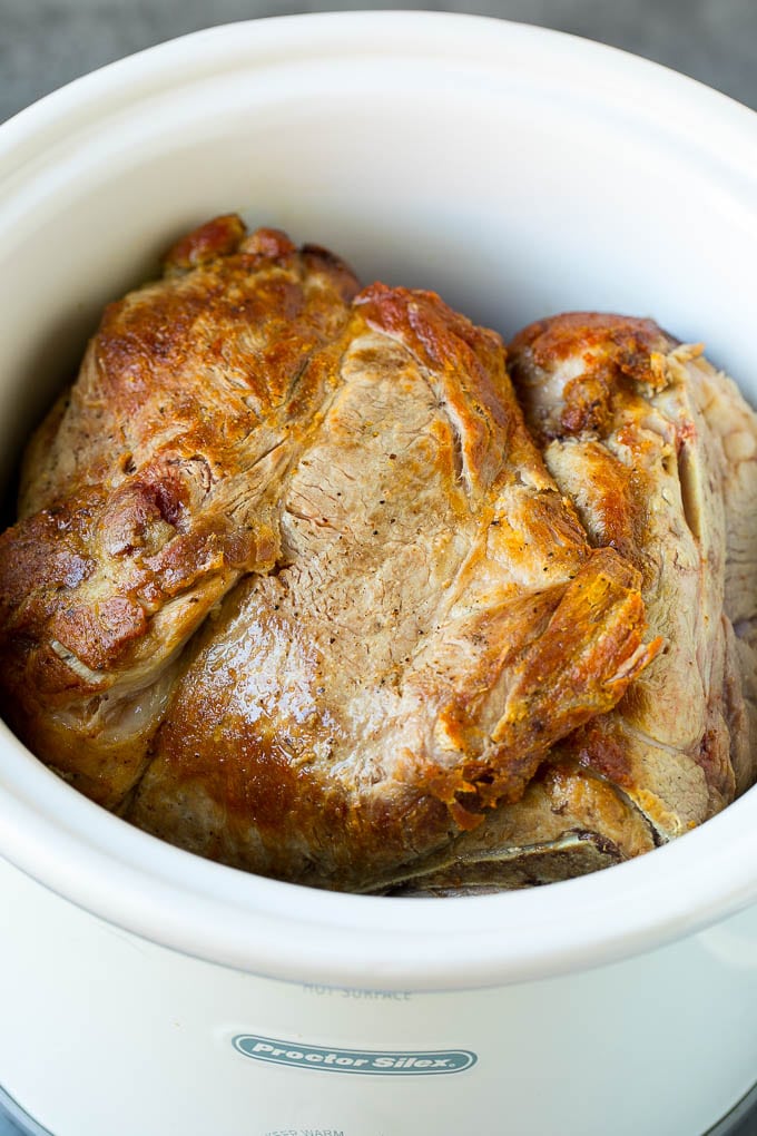 A seared pork shoulder roast inside of a slow cooker.