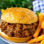 Slow cooker pulled pork on a hamburger bun, served with french fries.