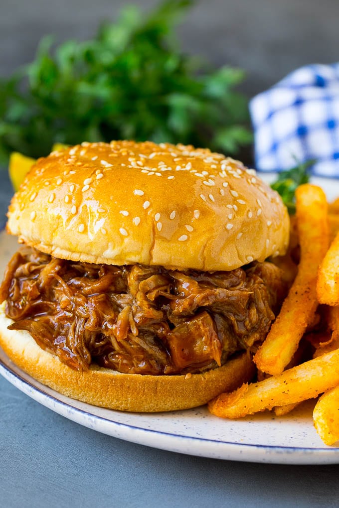 Slow cooker pulled pork on a hamburger bun, served with french fries.