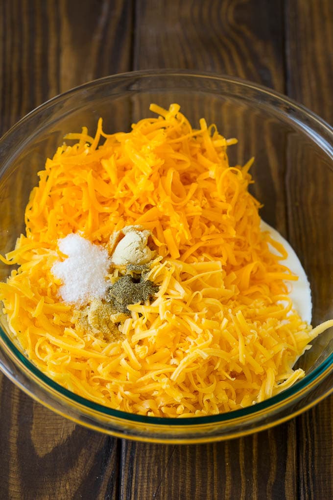 A bowl of milk, cream, two types of shredded cheese and seasonings.