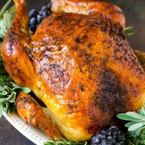 A whole roasted Thanksgiving turkey on a platter that's decorated with grapes and herbs.