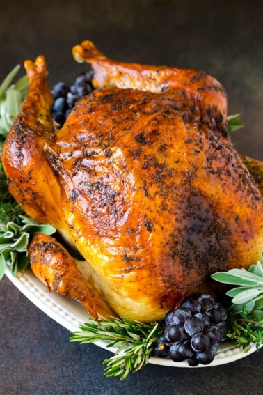 A whole roasted Thanksgiving turkey on a platter that's decorated with grapes and herbs.
