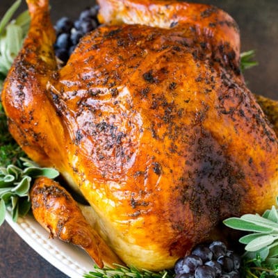 A whole roasted Thanksgiving turkey on a platter that's decorated with grapes and herbs.