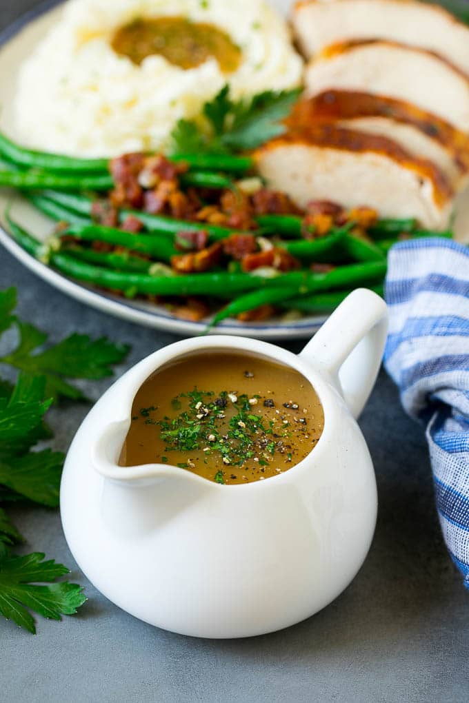 A pitcher of turkey gravy garnished with fresh parsley.