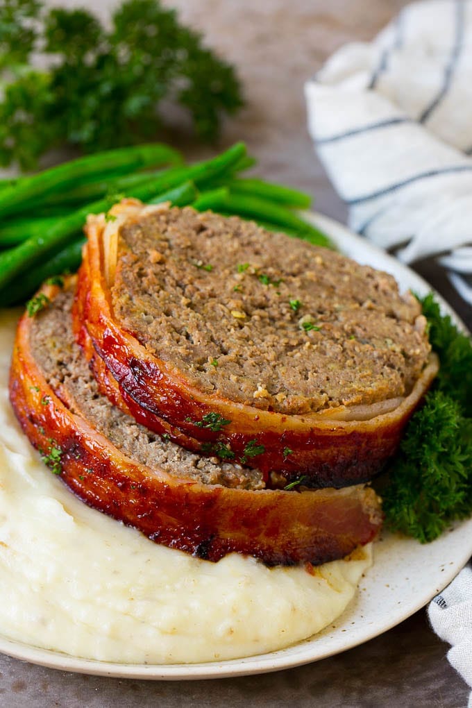 Slices of bacon wrapped meatloaf served over mashed potatoes with green beans.