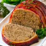 A bacon wrapped meatloaf with a slice out of it, on a serving platter.