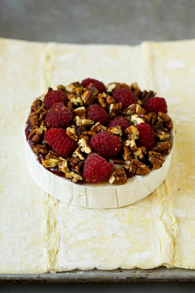 A wheel of brie cheese topped with jam, raspberries and pecans.