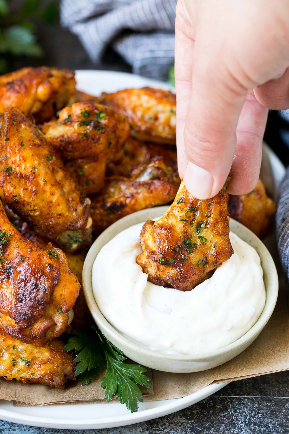 A hand dipping a chicken wing into ranch dip.