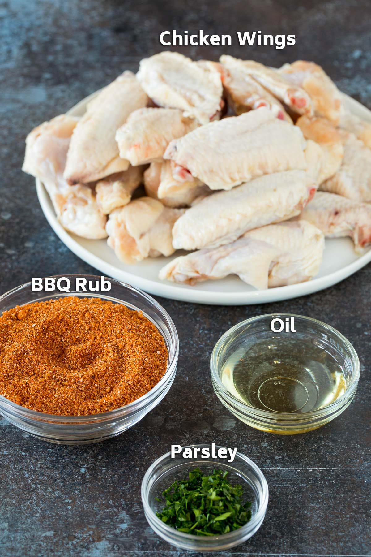 A plate of raw chicken and bowls of BBQ spice, parsley and oil.