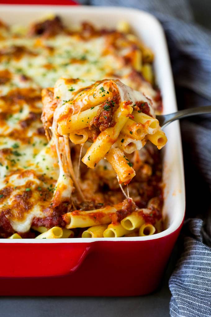 A spoon serving up a portion of baked ziti pasta.