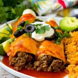 A plate of beef enchiladas topped with sour cream, olives and green onions.