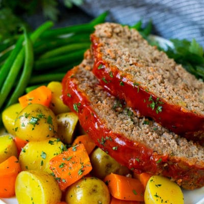 Slices of crockpot meatloaf served with carrots, potatoes and green beans.