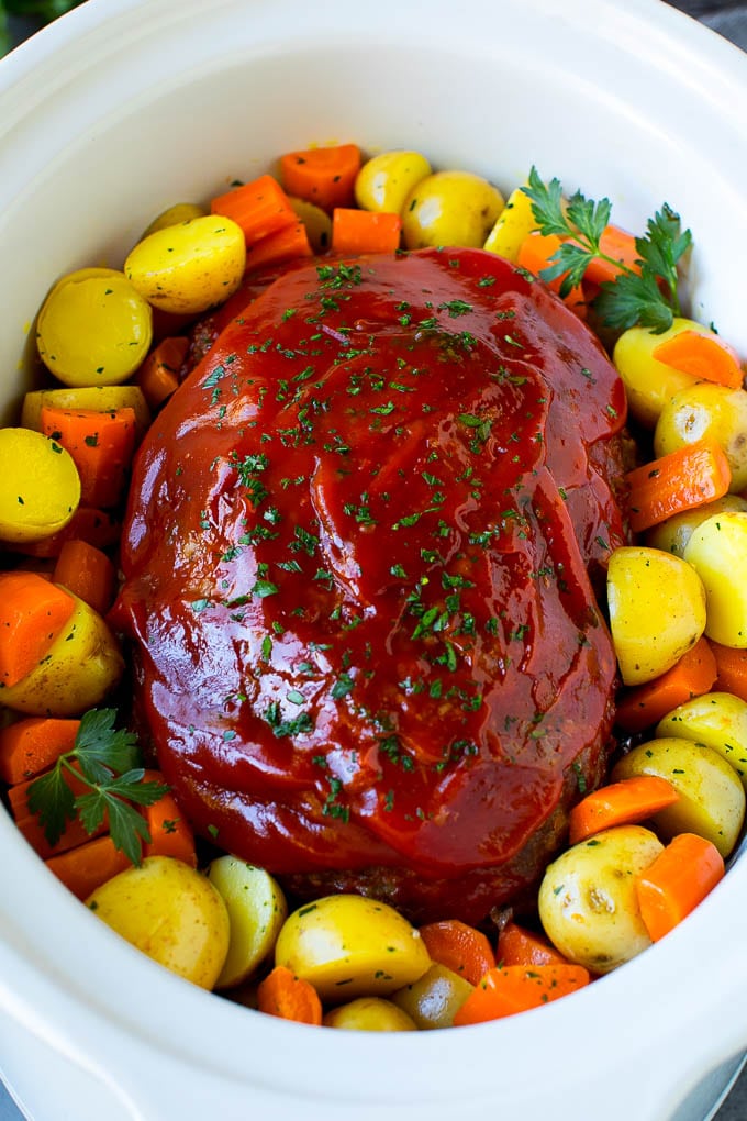 Crockpot meatloaf topped with ketchup and surrounded by carrots and potatoes.