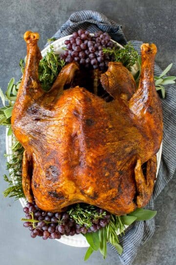 A whole deep fried turkey on a serving platter with herbs.