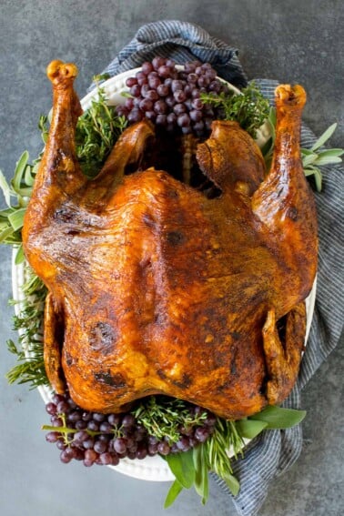 A whole deep fried turkey on a serving platter with herbs.