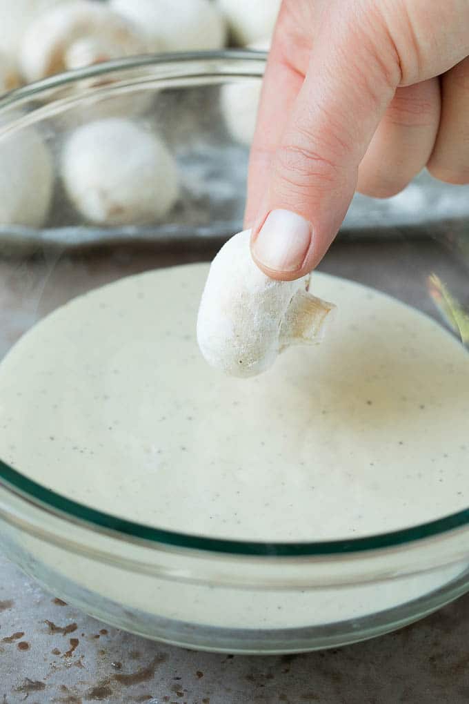 A mushroom being dipped into beer batter.