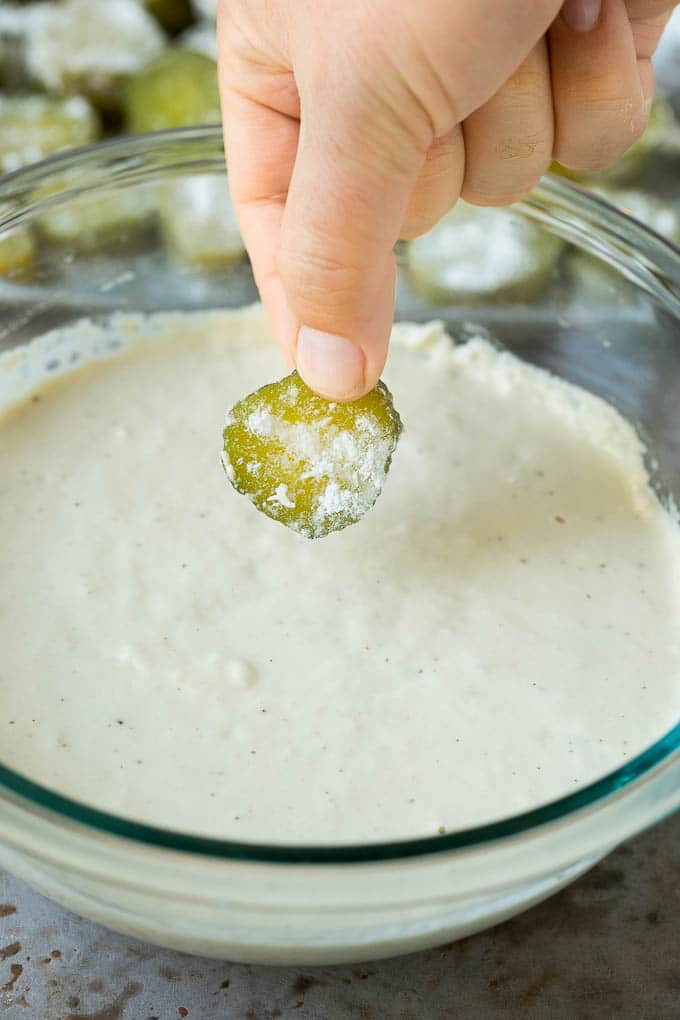 A pickle slice being dipped into a bowl of beer batter.