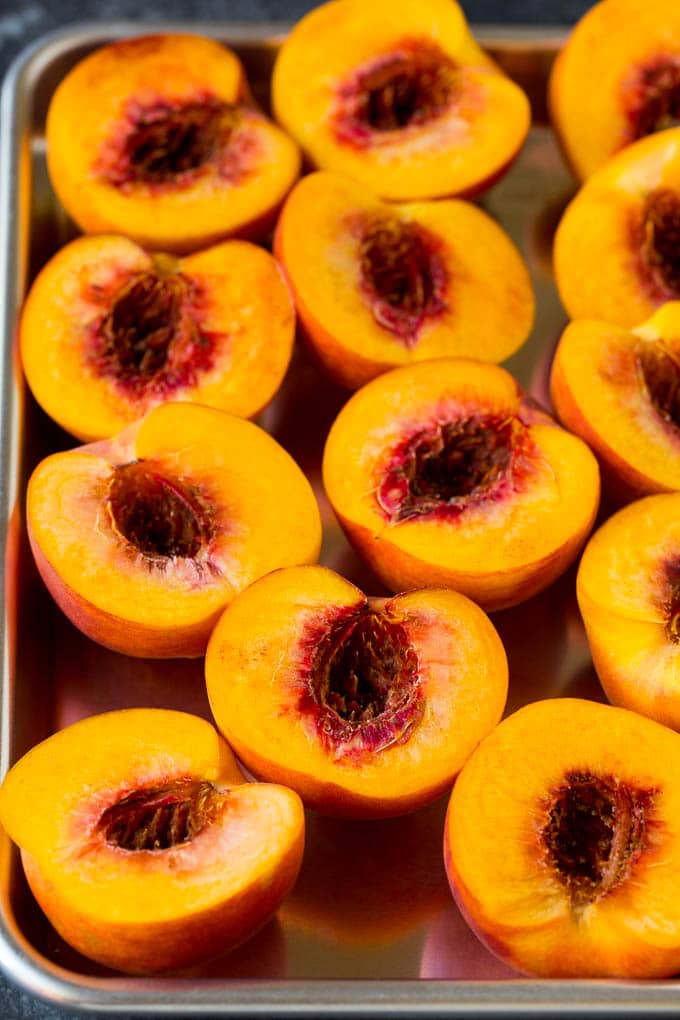 Peaches cut in half on a sheet pan.