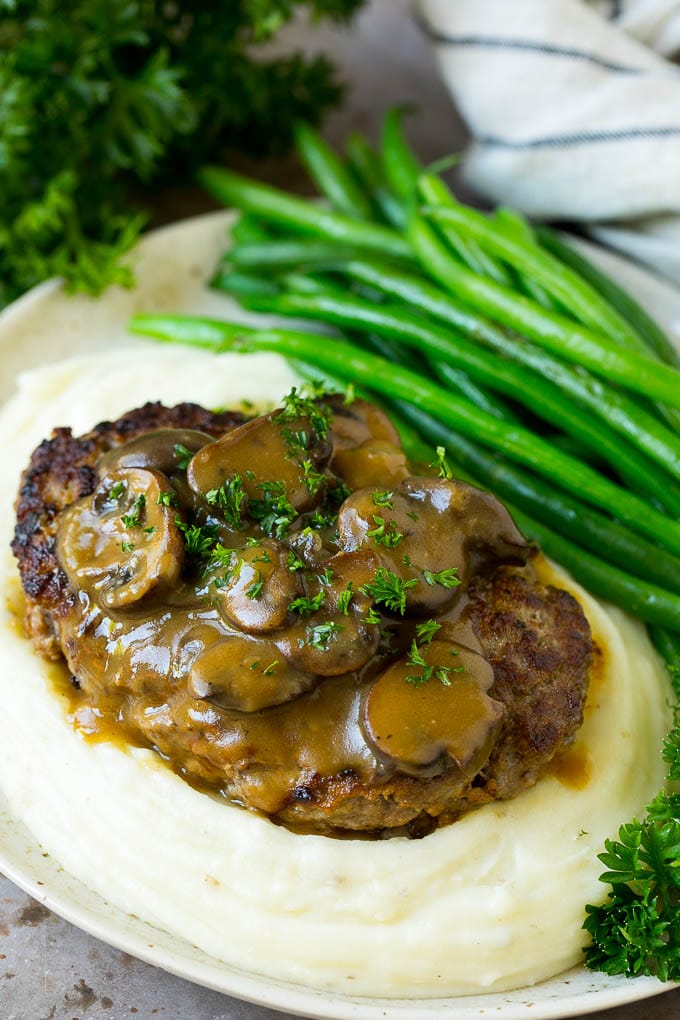 Hamburger steak served over mashed potatoes with green beans.