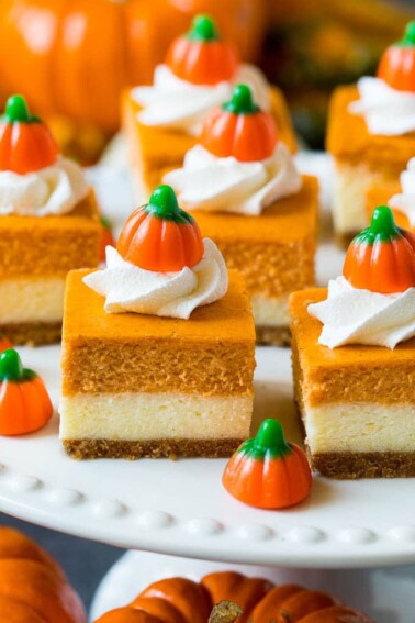 A platter of pumpkin cheesecake bars topped with whipped cream and candy pumpkins.