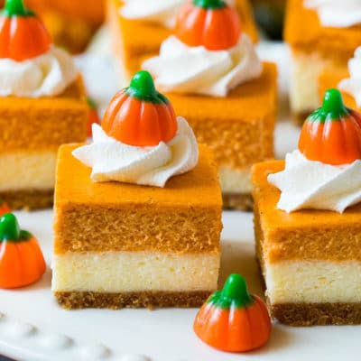 A platter of pumpkin cheesecake bars topped with whipped cream and candy pumpkins.