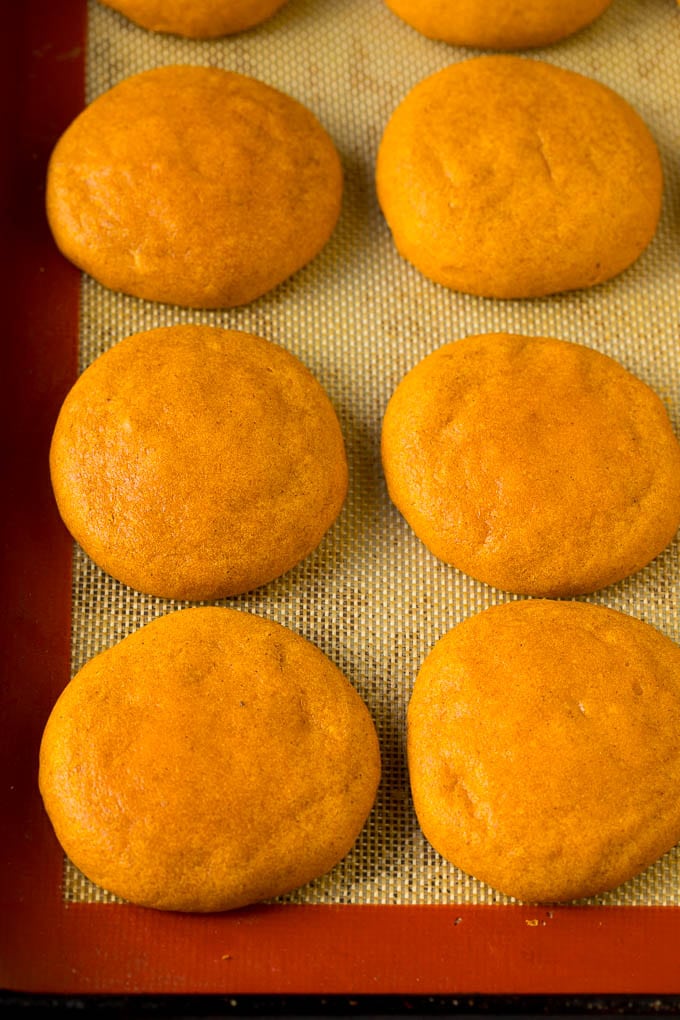These soft pumpkin cookies bake up light and fluffy, and are topped with a decadent cream cheese frosting and colorful sprinkles. Baked pumpkin cookies on a pan.