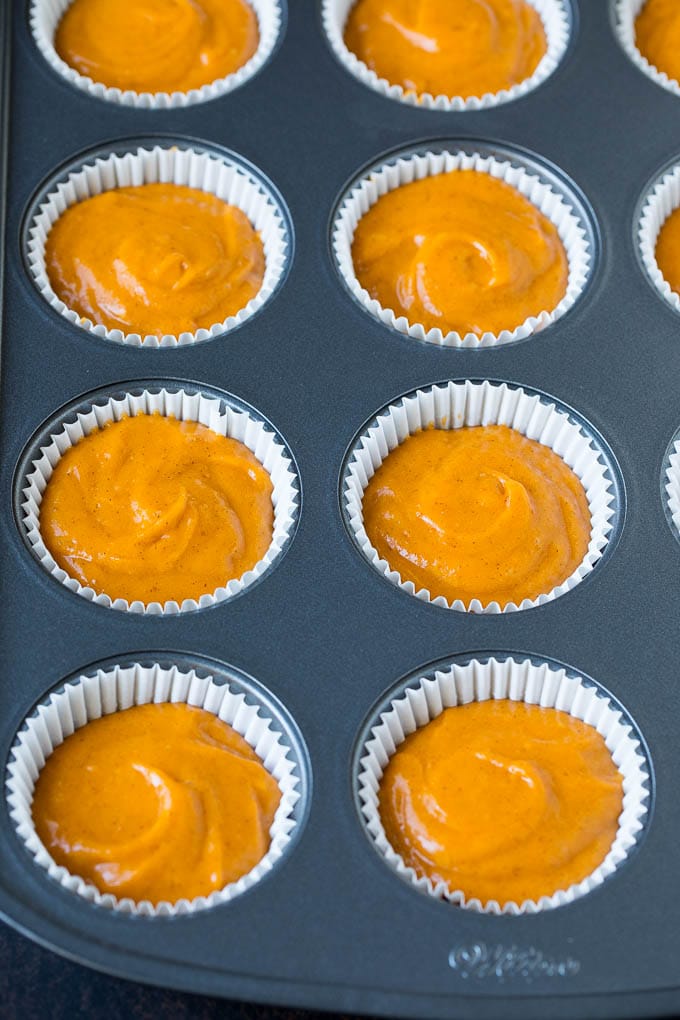 Pumpkin batter inside paper cups in a muffin tin.