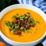 A bowl of pumpkin soup topped with bacon and pumpkin seeds.