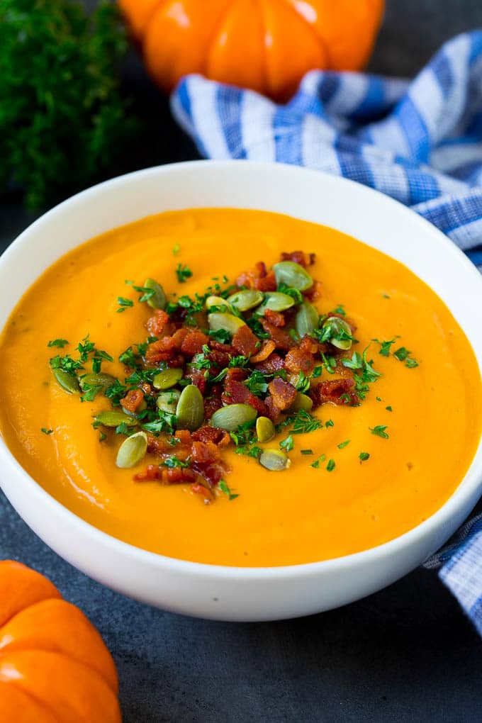 A bowl of pumpkin soup topped with bacon and pumpkin seeds.