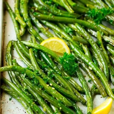 A pan of roasted green beans garnished with parsley and lemon.