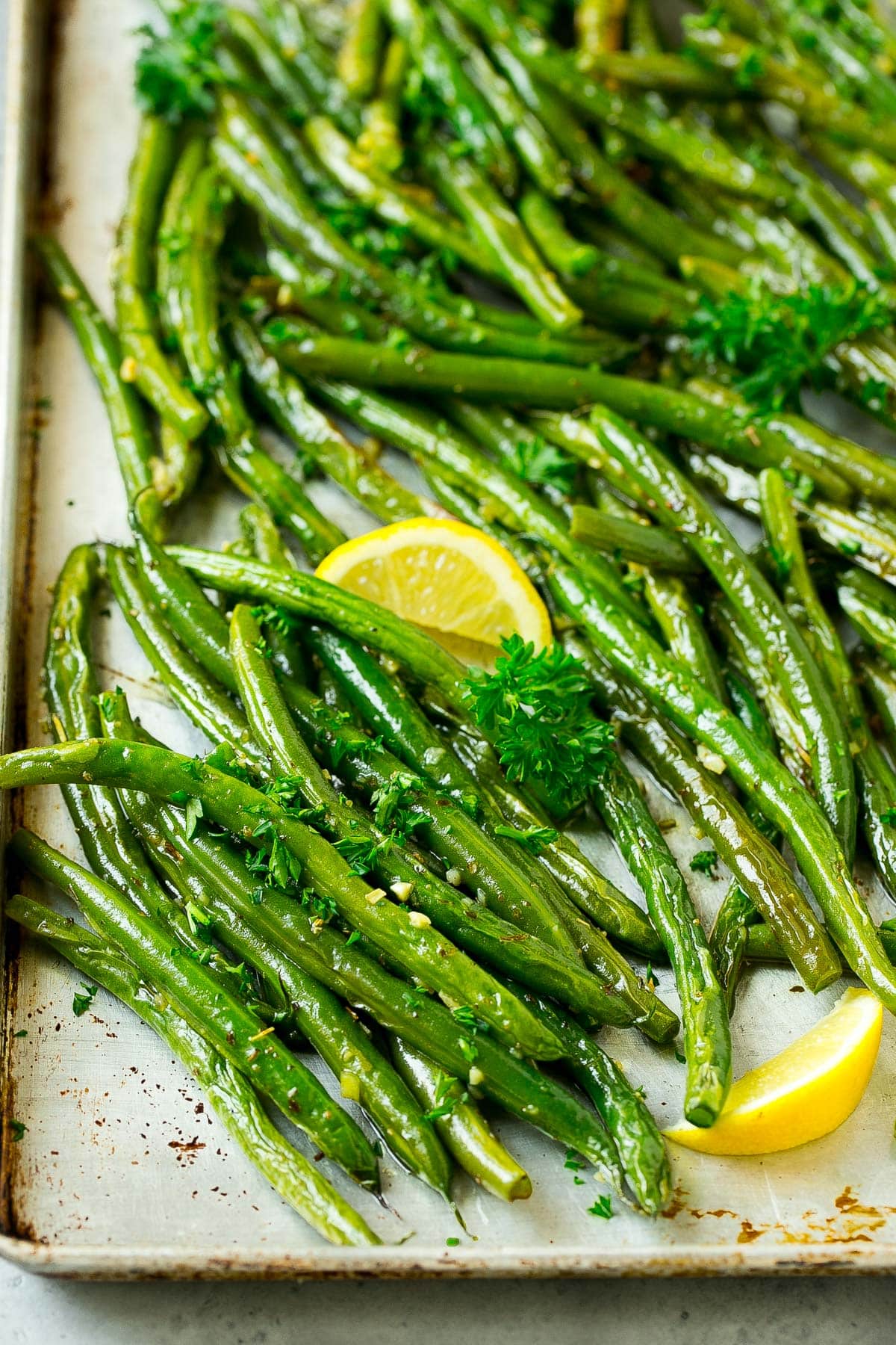 A pan of roasted green beans garnished with parsley and lemon.