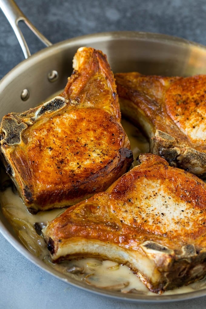 Pork chops on top of gravy in a pan.