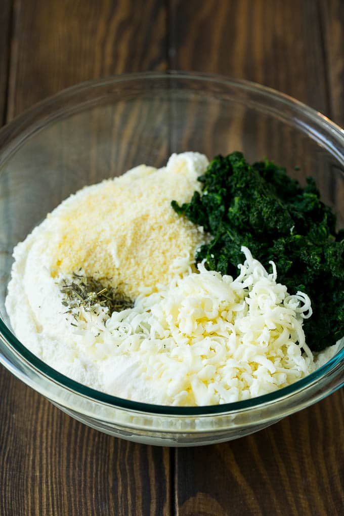 Three types of cheese, seasonings and freshly cooked spinach in a bowl.
