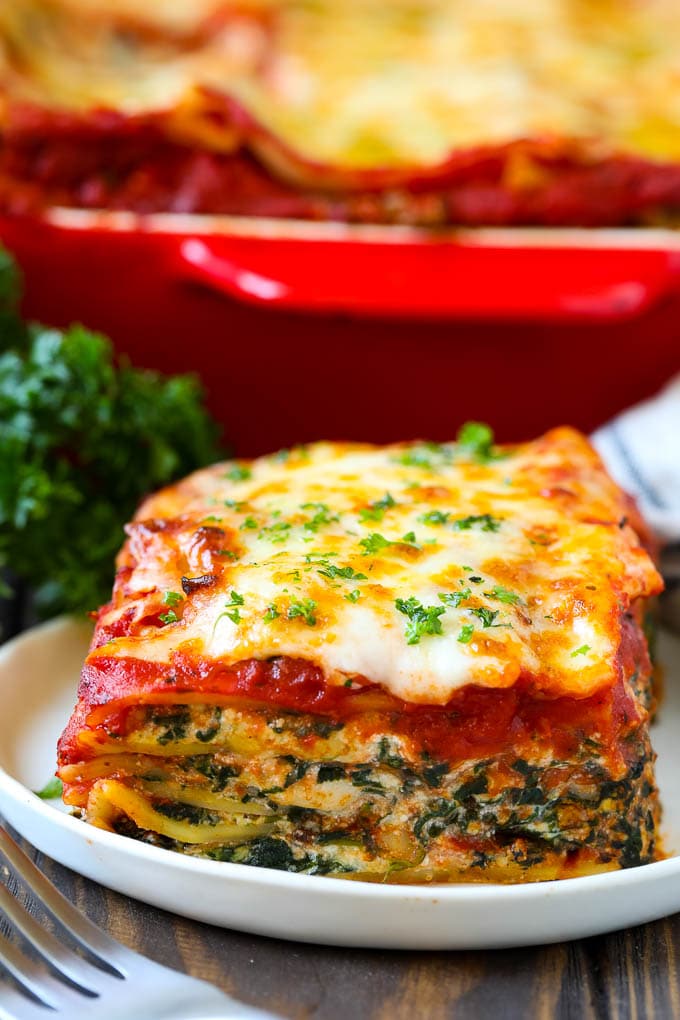 A piece of spinach lasagna on a plate, garnished with chopped parsley.