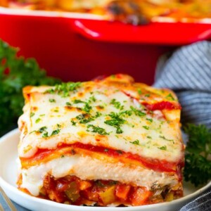A slice of vegetable lasagna topped with melted cheese and parsley.