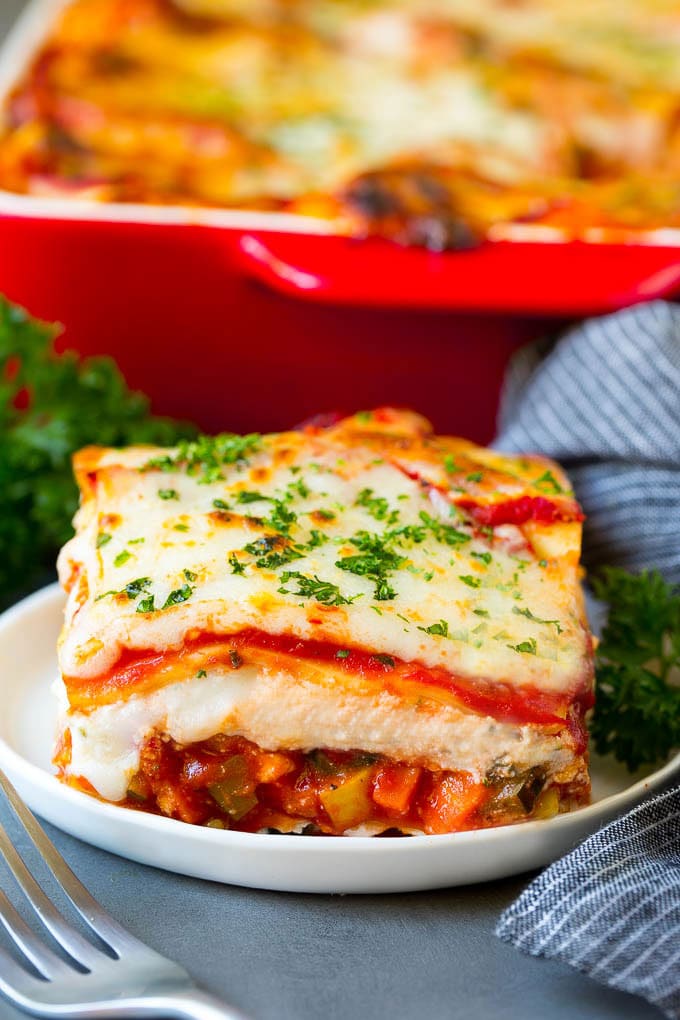 A slice of vegetable lasagna topped with melted cheese and parsley.