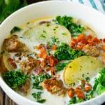 A bowl of zuppa toscana soup with sausage, potatoes, bacon and kale.