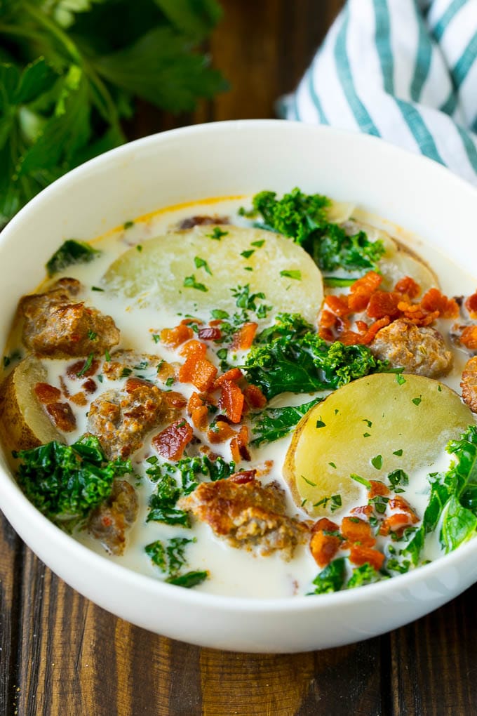 A bowl of zuppa toscana soup with sausage, potatoes, bacon and kale.