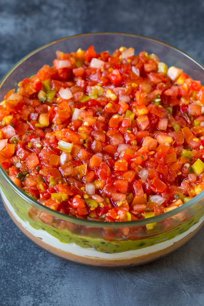 Layers of beans, sour cream, guacamole and salsa in a glass bowl.