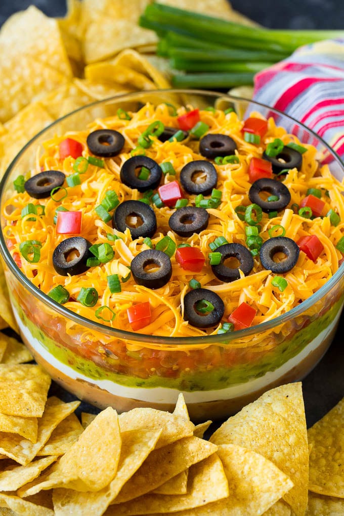 A bowl of 7 layer dip surrounded with tortilla chips.