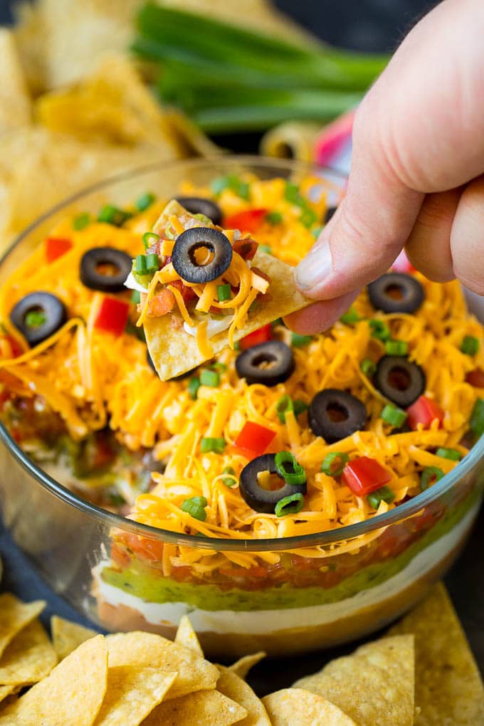 A hand scooping out a serving of 7 layer dip.