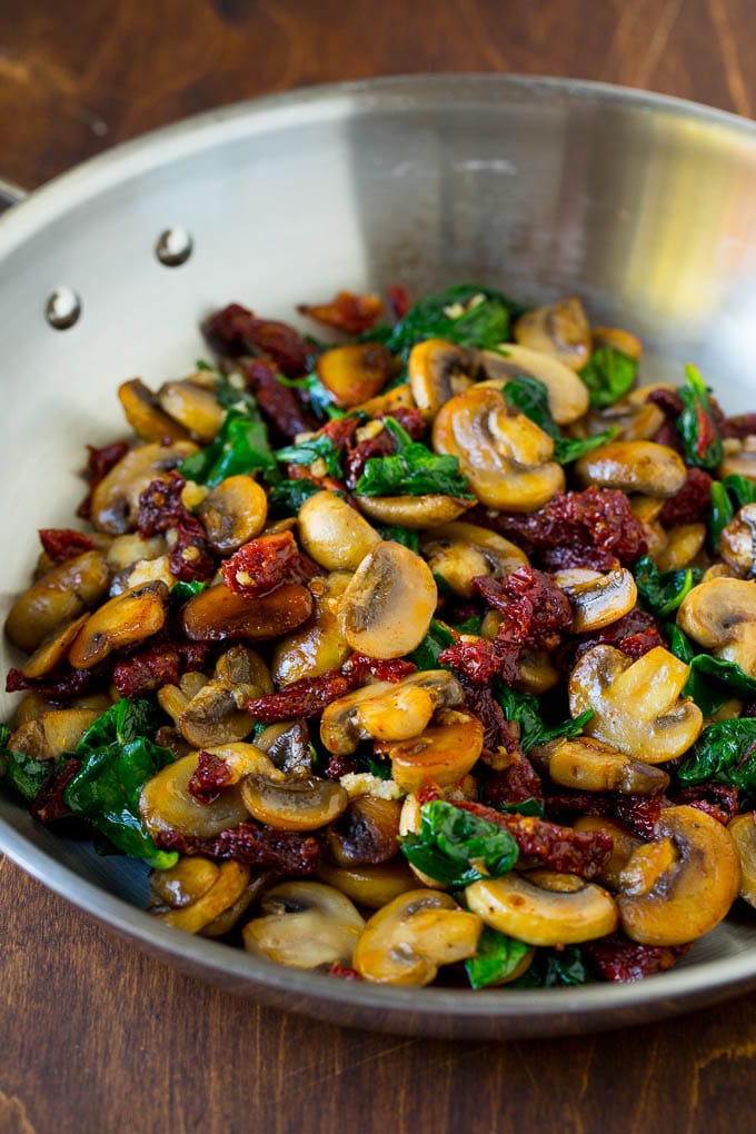 A pan of sauteed mushrooms, garlic, spinach and sun dried tomatoes.