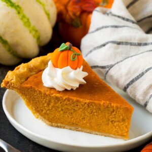 A slice of homemade pumpkin pie topped with whipped cream and a candy pumpkin.