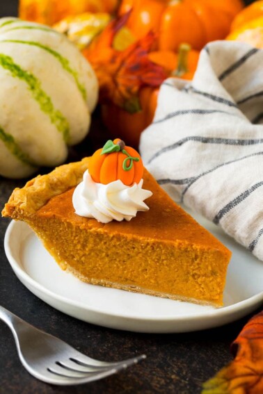 A slice of homemade pumpkin pie topped with whipped cream and a candy pumpkin.