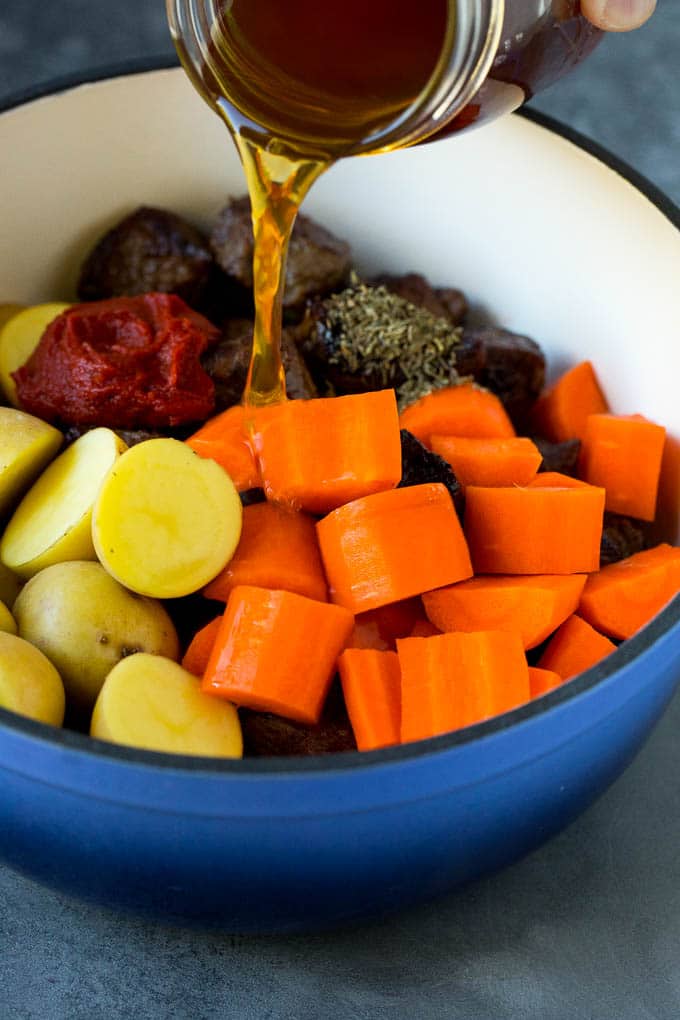 Broth being poured into a pot of carrots, potatoes and beef.