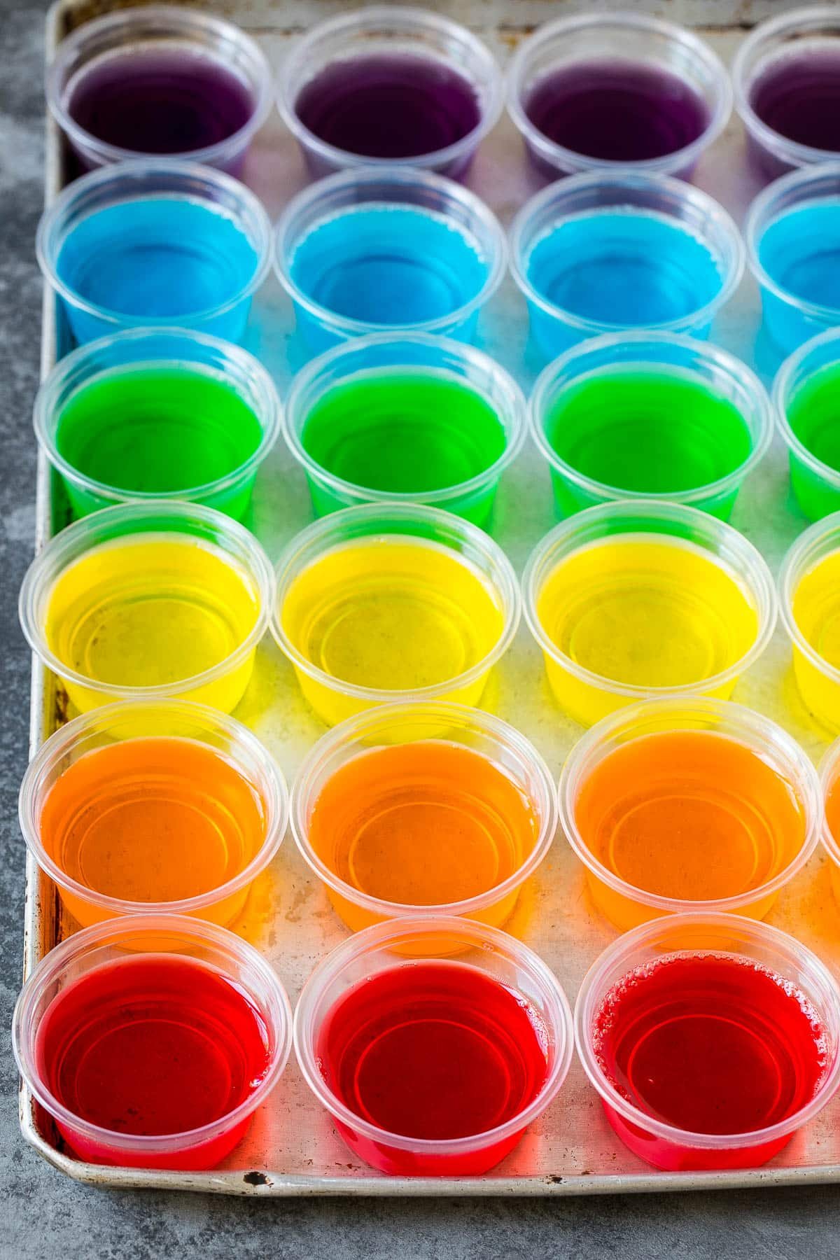 Rows of rainbow colored Jello shots lined up on a sheet pan.