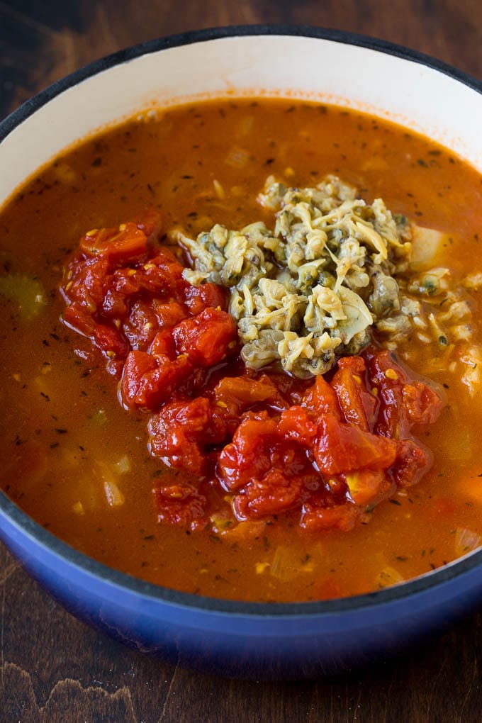 A pot of broth topped with tomatoes and baby clams.