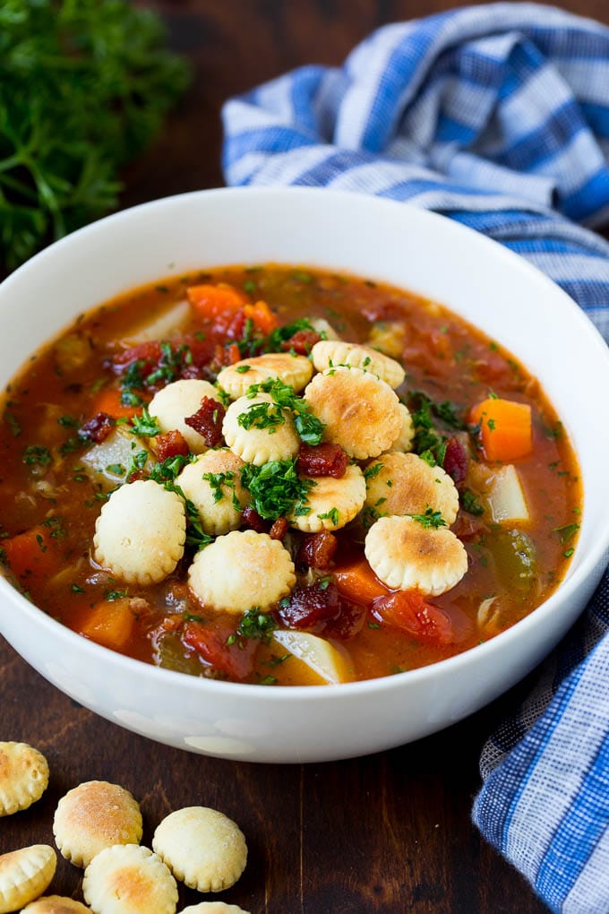 A bowl of Manhattan clam chowder topped with crackers, bacon and parsley.