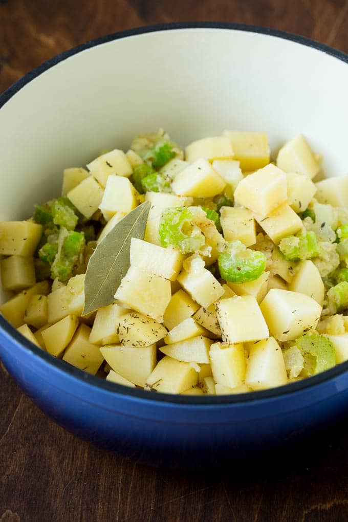 Potatoes, celery, herbs and onion in a pot.